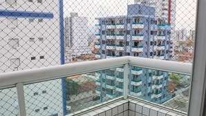 Une vue depuis un balcon, avec une clôture en treillis métallique, donnant sur un immeuble à plusieurs étages, lui aussi doté de balcons.