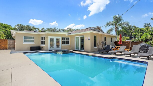 Un jardin avec une piscine, un patio couvert et une maison avec une porte et des fenêtres.
