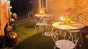 An outdoor patio with metal chairs and tables, a small potted plant, and a vase with flowers.