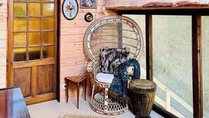 A cozy room with wooden walls, a large window, a woven chair, a small table, and a decorative fan.