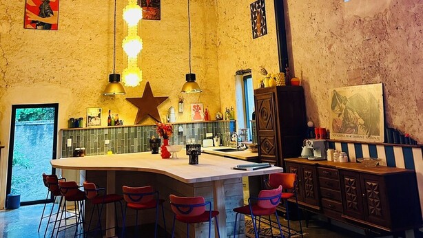 A rustic kitchen with a wooden ceiling, a bar area with red bar stools, and a large window.