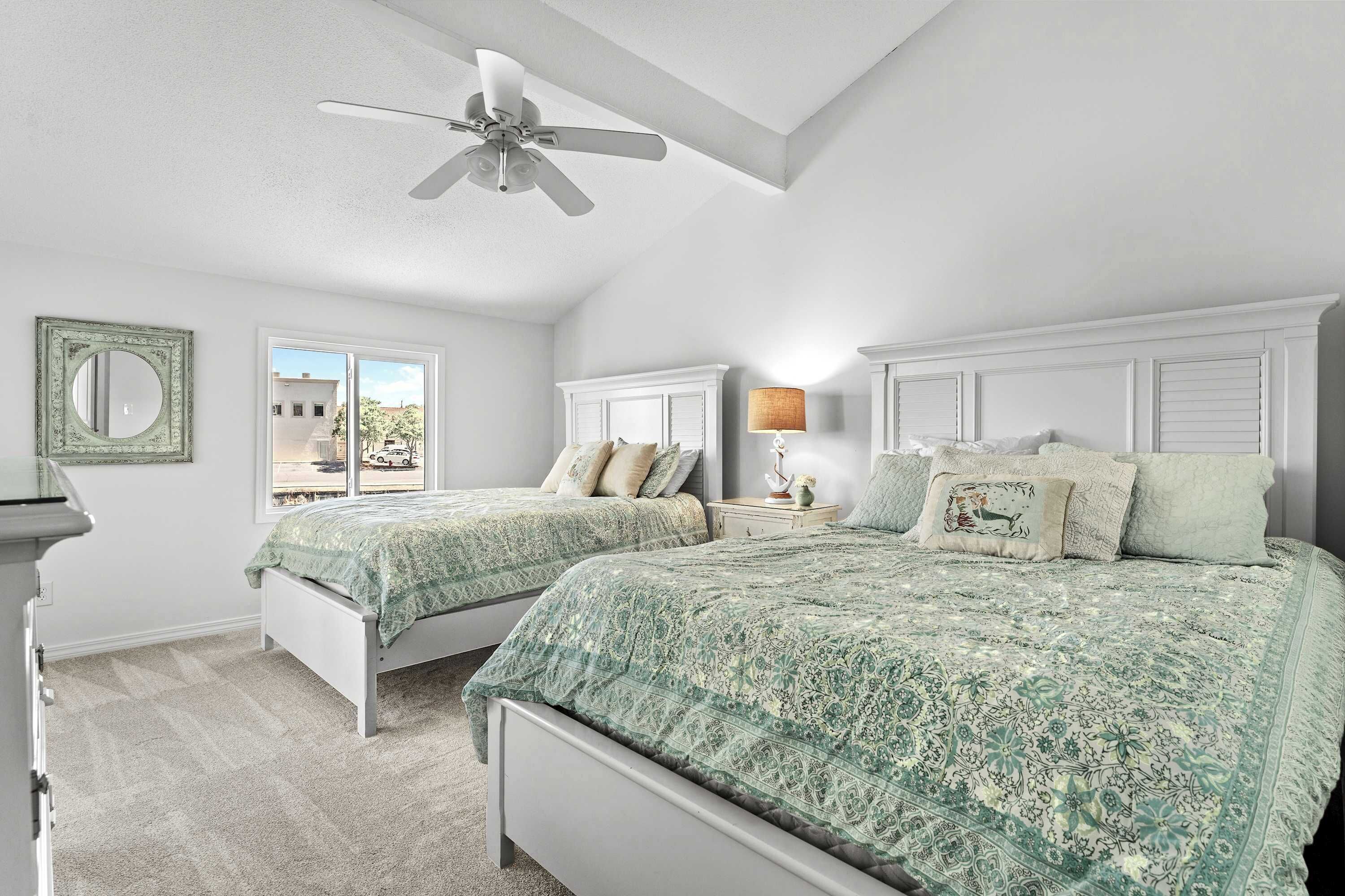 A bedroom with two beds, a ceiling fan, and a window with a view of buildings.