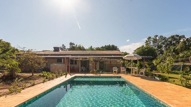 A swimming pool with a tiled deck, a covered patio area, and a building with a tiled roof in the background.