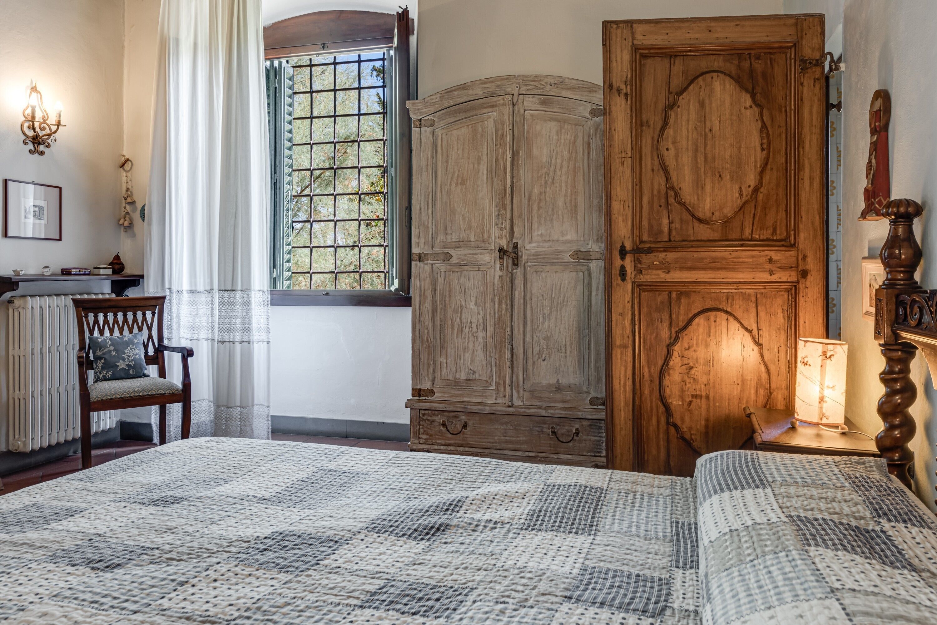 Une chambre avec un grand lit, une armoire en bois, une chaise, une fenêtre donnant sur un beau paysage et une table de chevet avec une lampe.