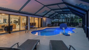 A modern outdoor pool area with lounge chairs, a glass-enclosed patio, and a view of the interior living spaces.