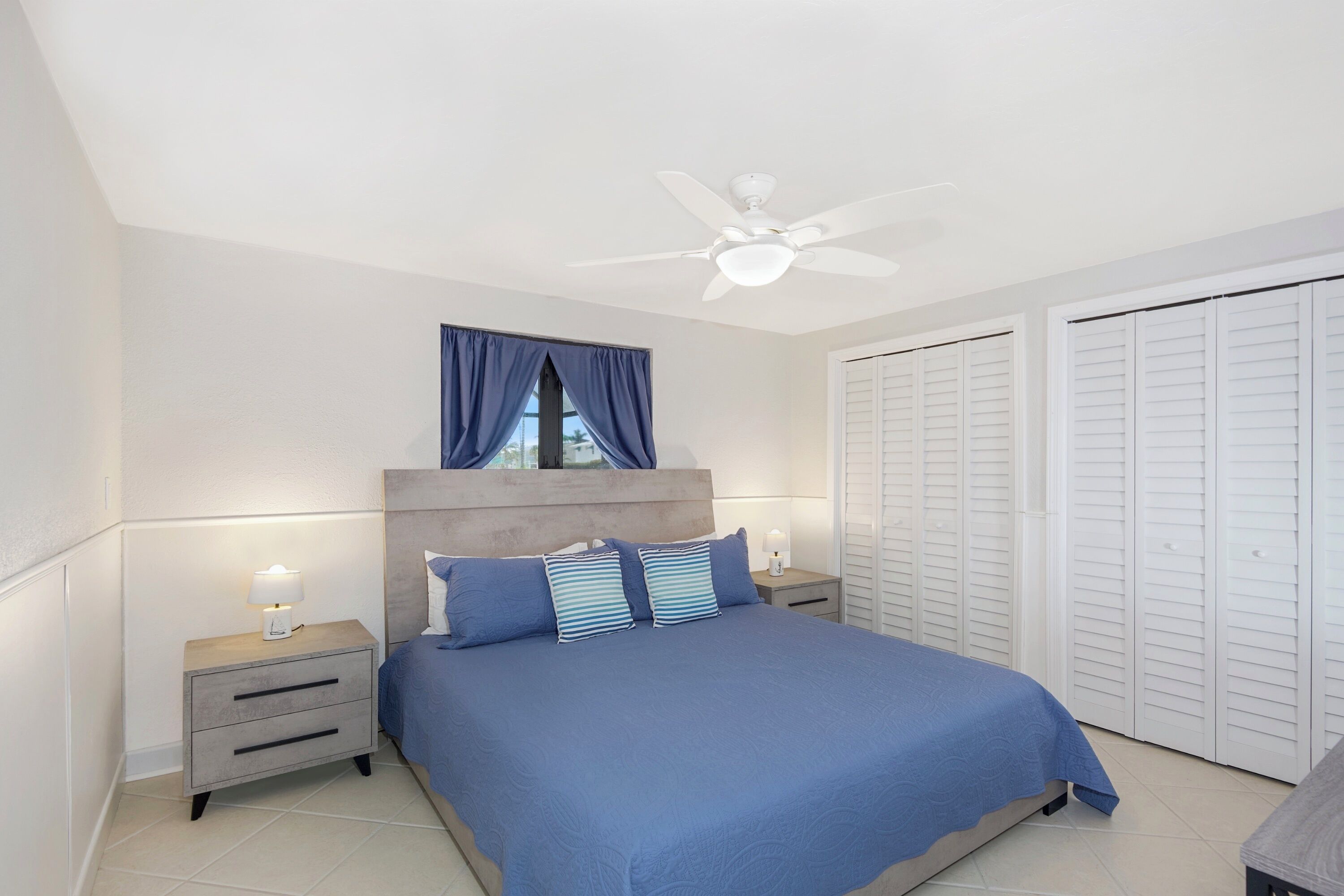 A bedroom with a bed, nightstands, a ceiling fan, and a window with curtains.