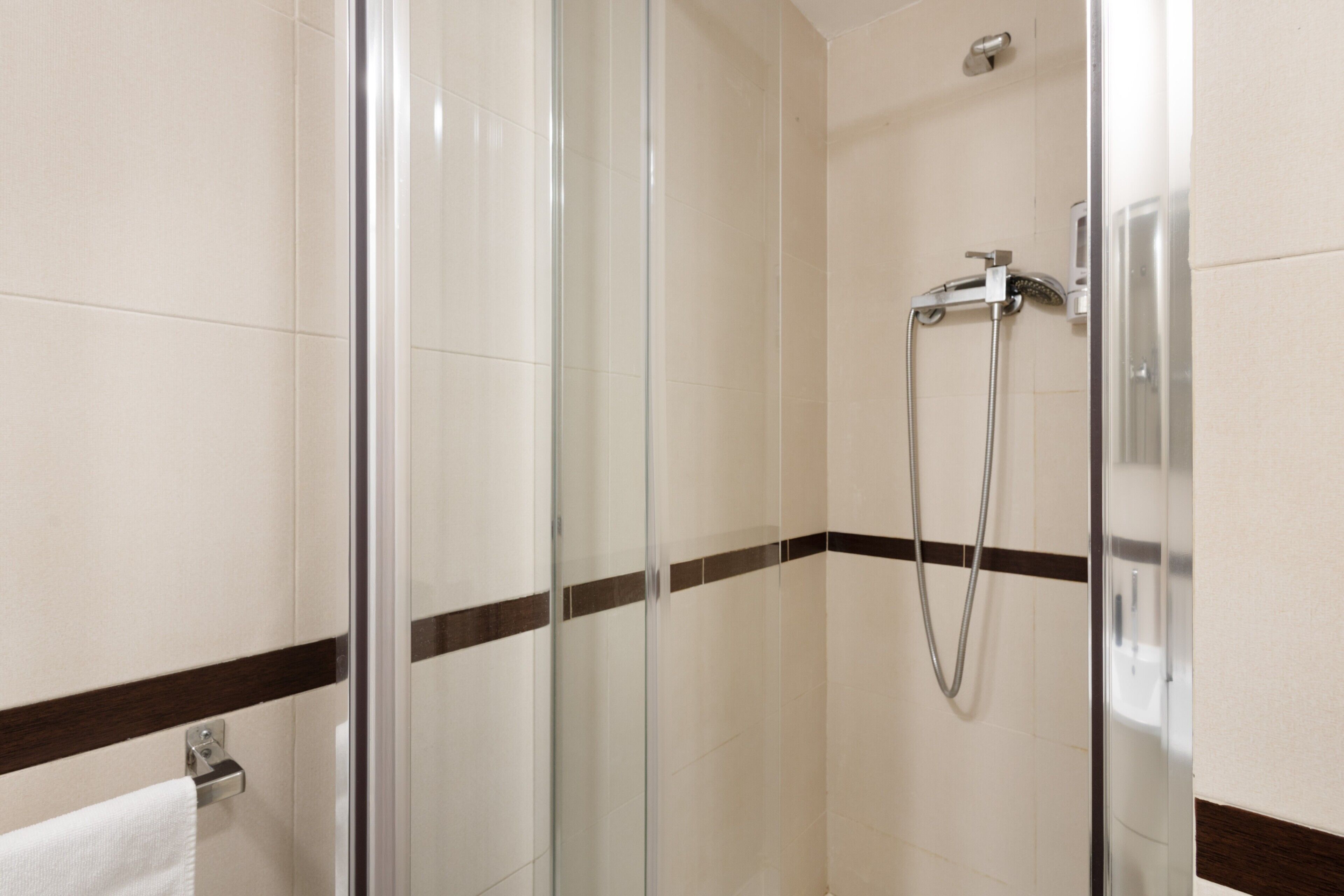 Une douche fermée par des parois en verre, dotée d’un pommeau de douche à main, d’un porte-serviettes et d’une serviette fixée au mur.