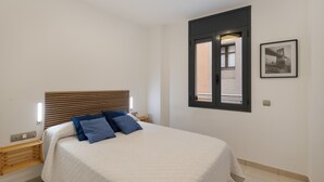 Ein Schlafzimmer mit Bett, Holz-Kopfteil, Fenster mit Blick und einem gerahmten Bild an der Wand.