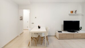 Ein modernes Wohnzimmer mit einem weißen Esstisch, Stühlen, einem Flachbildfernseher und einer schlichten Kommode.