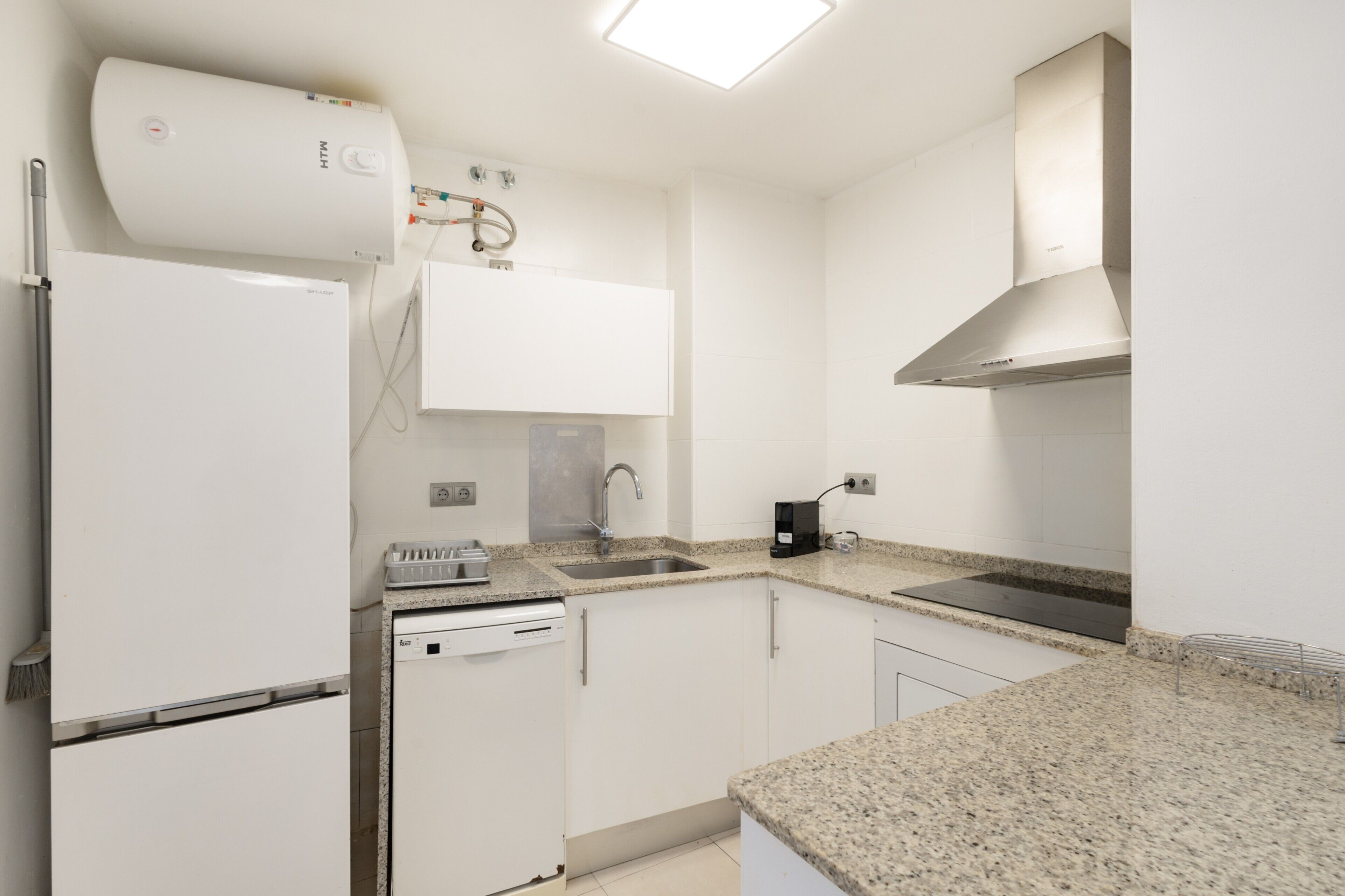 Una cocina moderna con armarios blancos, lavavajillas integrado, pileta de acero inoxidable y cocina a gas.