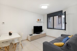 A modern living room with a flat-screen TV, a sofa with cushions, a dining table with chairs, and a window with a view of the outside. - Apartment 'Puig Cardener 1' with Wi-Fi (Manresa)