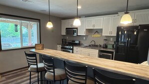 A modern kitchen with white cabinets, a black refrigerator, a wooden island with bar stools, and pendant lighting.