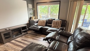 A living room with a large leather sofa, a flat-screen TV, and a window with curtains.
