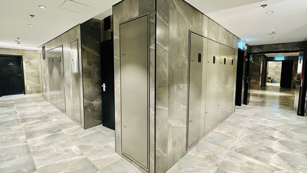 Un hall d’ascenseur moderne, avec des murs et des sols en marbre, et un ascenseur central doté d’une porte noire.