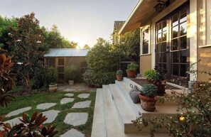 A garden with stone steps leading to a house with large windows and a metal roof.