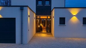 A modern two-story house with a driveway leading to a glass door entrance. - Maison du lac, 1h from Lyon and Genèves, Jacuzzy, swimming pools, magnificent lake view. (Jayat)