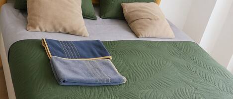 A bed with a green quilt, two green pillows, and a beige pillow.