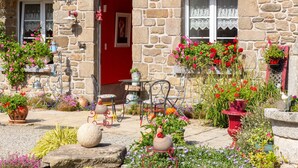 A stone building with a red door and windows, outdoor seating, and potted plants. - Holiday Home 'Les Géraniums À 800m Plage' with Private Terrace, Shared Garden and Wi-Fi (Kerlaz)