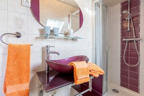 A bathroom with a glass sink, a towel rack with an orange towel, a shower with a glass door, and a mirror above the sink. - Holiday Home 'Les Géraniums À 800m Plage' with Private Terrace, Shared Garden and Wi-Fi (Kerlaz)