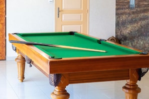 Una mesa de billar con taco y una bola, patas de madera y superficie con fieltro verde.