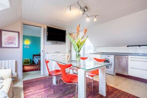 A modern kitchen with white cabinets, a glass dining table, and red chairs. - Holiday Home 'Les Géraniums À 800m Plage' with Private Terrace, Shared Garden and Wi-Fi (Kerlaz)