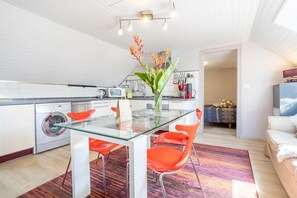 Una cucina moderna con un tavolo da pranzo in vetro, sedie rosse, una lavatrice e un divano nella zona giorno.