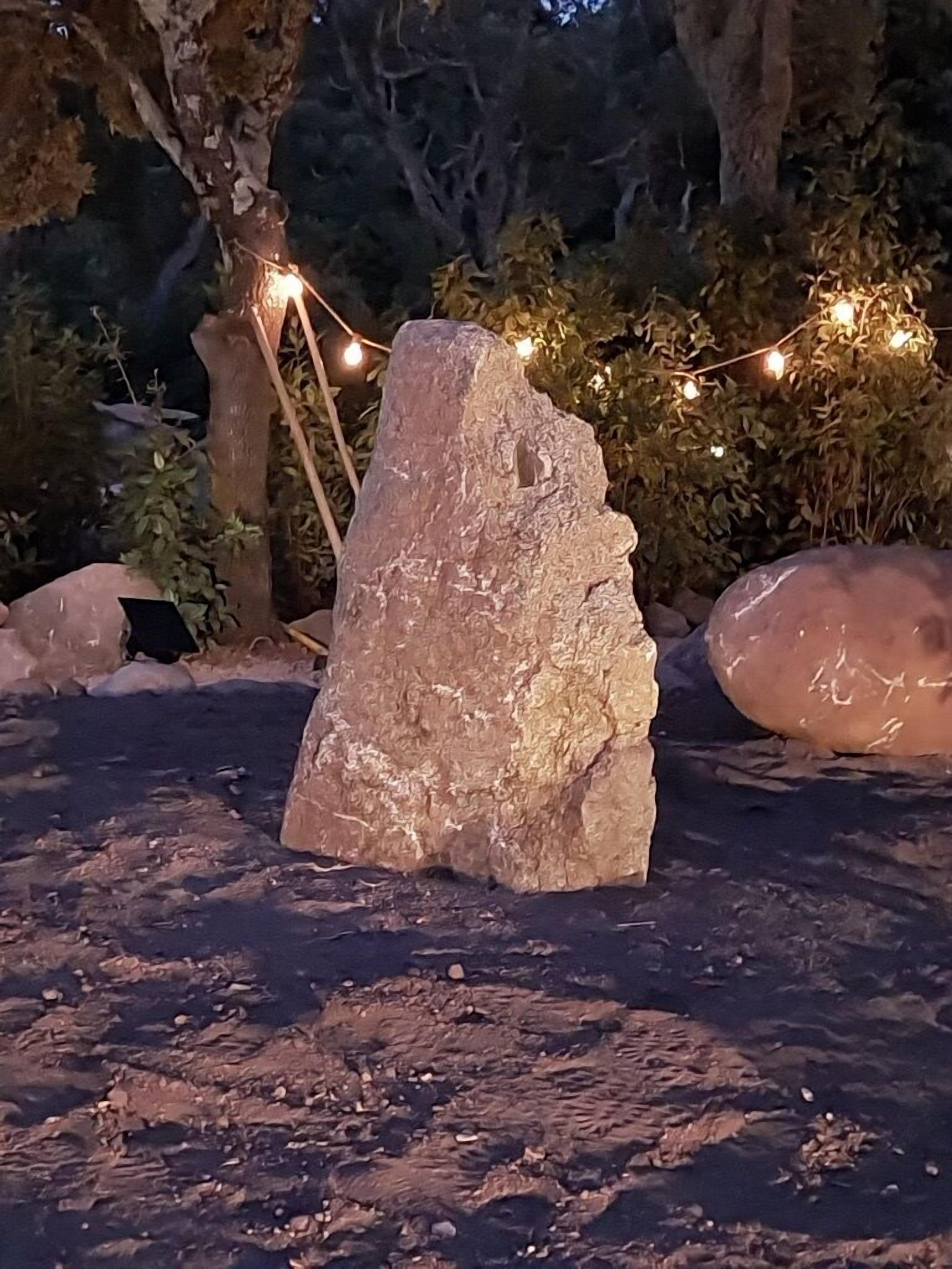 Une grande formation rocheuse dans un environnement naturel, avec des guirlandes lumineuses en arrière-plan.