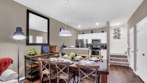 Une cuisine moderne avec des meubles blancs, un coin repas avec des chaises en bois et un escalier menant à un autre niveau.