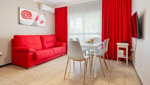 Een moderne woonkamer met een rode bank, een witte eettafel met stoelen, een flatscreen televisie en een schilderij aan de muur.