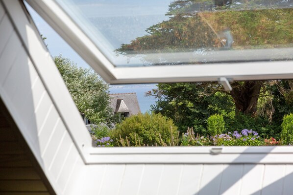 Ein Dachfenster mit Blick auf einen Garten, einen Baum und ein Gebäude mit geneigtem Dach.