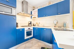 Une cuisine avec des meubles bleus, un plan de travail blanc, un four à micro-ondes, une cuisinière et une machine à café.
