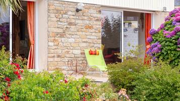 A stone building with a glass door, a green chair outside, and a garden with various plants and flowers.