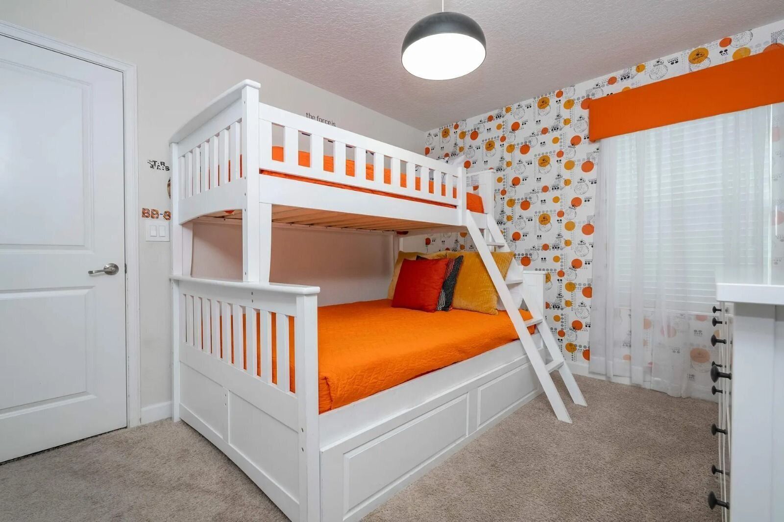 A bunk bed with orange bedding, a ladder, and a white door.