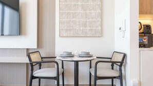 A modern dining area with a round table, two chairs, and a wall-mounted TV. - StayShort - Town Square Stylish Studio for 2 people! (Town Square)