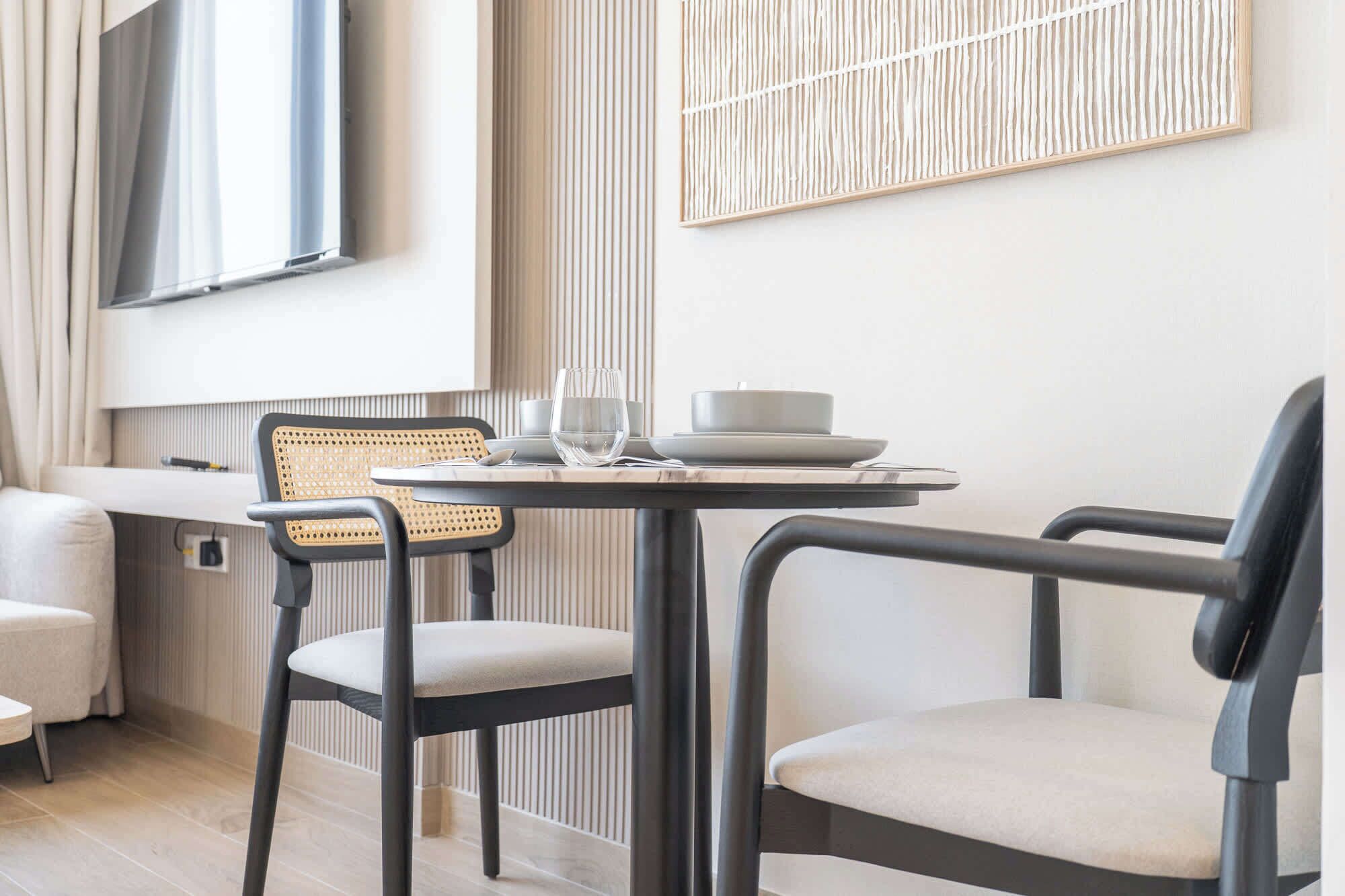 A modern dining area with a table set for two, featuring a minimalist design with a woven chair and a sleek chair.