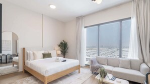A modern hotel room with a large bed, a sofa, a small table, and a view of the city through large windows. - StayShort - Town Square Stylish Studio for 2 people! (Town Square)