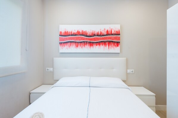 A bedroom with a white bed, a white headboard, a white nightstand, and a red abstract painting on the wall.