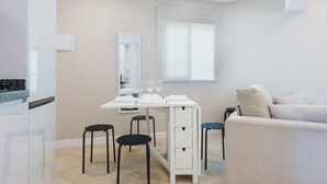 A modern living room with a white sofa, a dining table with chairs, and a kitchen area with a refrigerator.