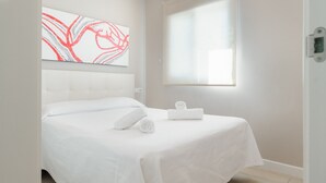A hotel room with a bed, a window with blinds, a wall-mounted artwork, and a bedside table with a towel.