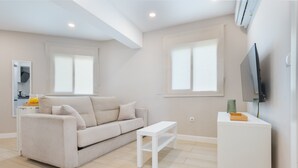 A modern living room with a sofa, a coffee table, a TV on a stand, and a window with blinds.