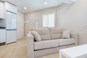 Ein modernes Wohnzimmer mit einem beigen Sofa, einem weißen Couchtisch und einer Küchenzeile mit einem weißen Kühlschrank.