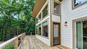 Une terrasse en bois avec une rambarde, de grandes fenêtres et une porte donnant sur un espace abrité.