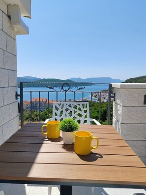 Ein Balkon mit einem Holztisch, zwei gelben Tassen und einem Blumentopf.