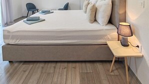 A modern hotel room with a large bed, a bedside table with a lamp, a flat-screen TV mounted on the wall, and a chair. - Apartment with Sea and Nature view (Neum)