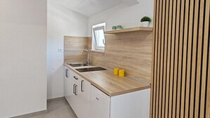 A compact kitchen with white cabinetry, a wooden countertop, and a built-in sink. There is a window above the sink and a small plant on the countertop. - Apartment with Sea and Nature view (Neum)