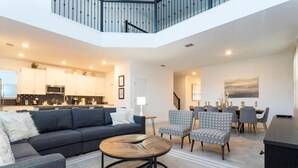 Un área de estar moderna y de concepto abierto con cocina, comedor y una escalera a un nivel superior.