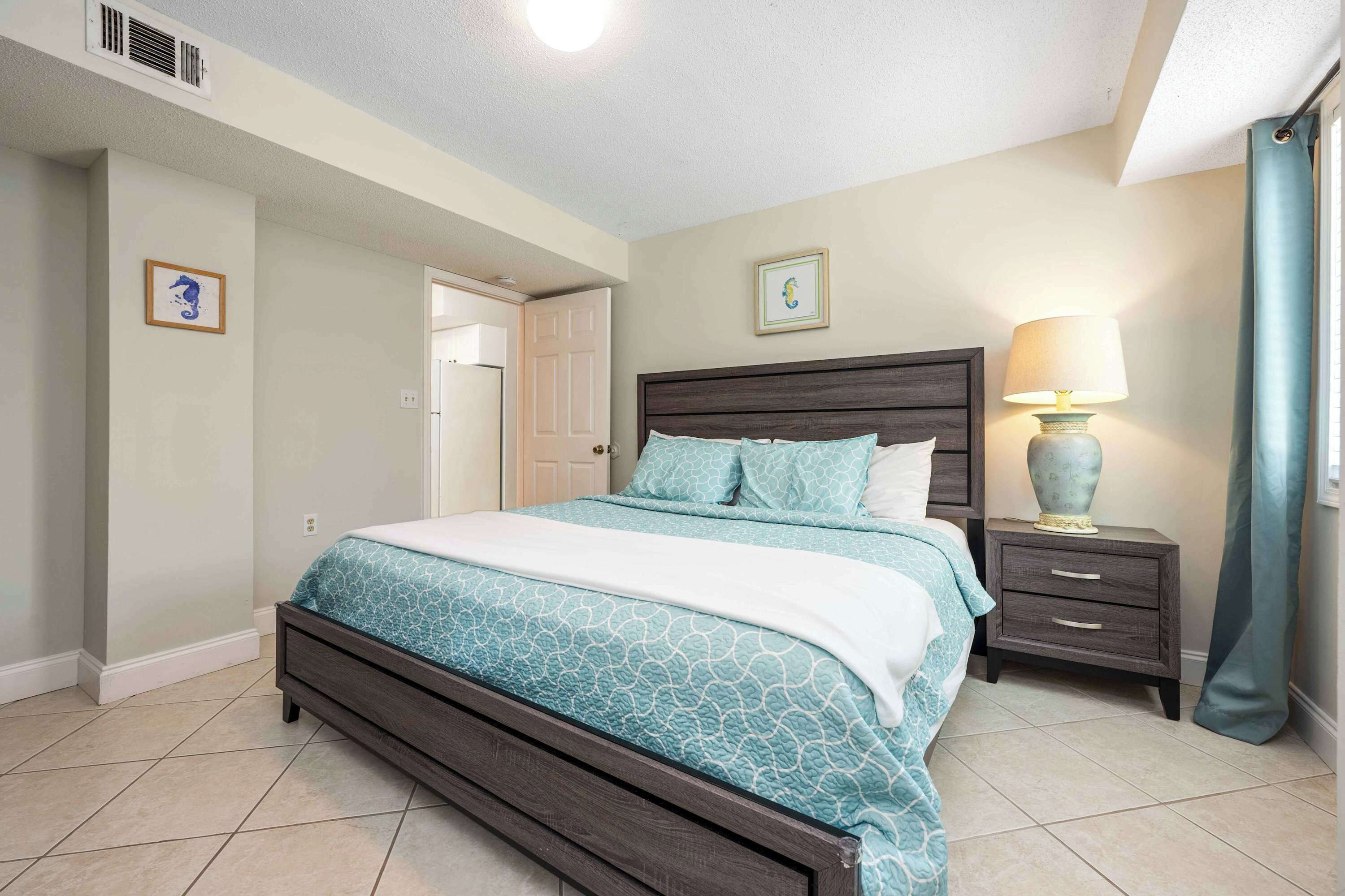 A bedroom with a bed, bedside table, lamp, and two framed pictures on the wall.