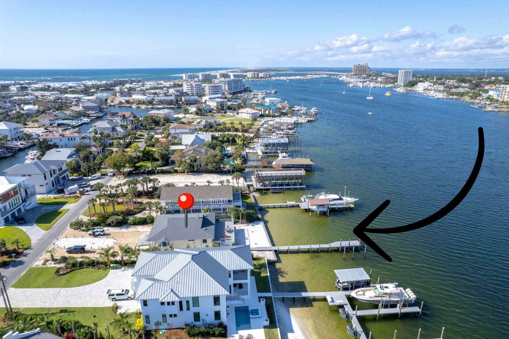 An aerial view of a coastal town with a marina, houses, and a prominent white building with a red location marker.