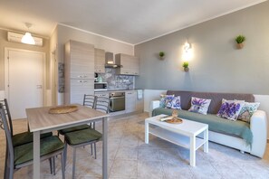 A modern kitchen with built-in appliances, a dining area with a table and chairs, and a living area with a sofa and cushions.