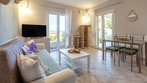 A living room with a sofa, a coffee table, a TV, a dining table with chairs, and a balcony door.